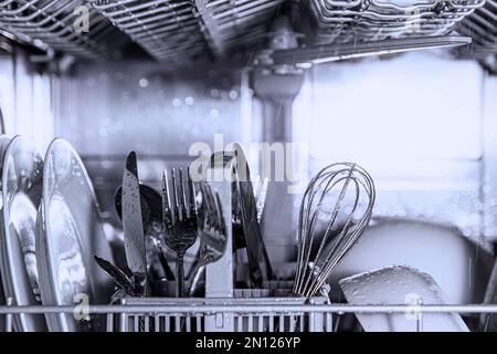 Frontansicht der offenen automatischen Edelstahl-Einbaumaschine mit vollständig integrierter Top-Control-Spülmaschine mit sauberen Utensilien, Besteck, Gläsern, Geschirr, Tellern in der modernen Wohnküche Stockfoto