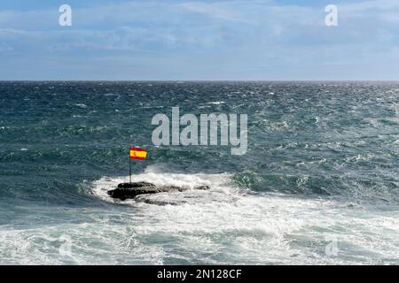 Eine spanische Flagge auf Felsen im Atlantik bei windigem Wetter in der Bucht von Pozo Izquierdo, Gran Canaria, den Kanarischen Inseln, Spanien und Europa Stockfoto