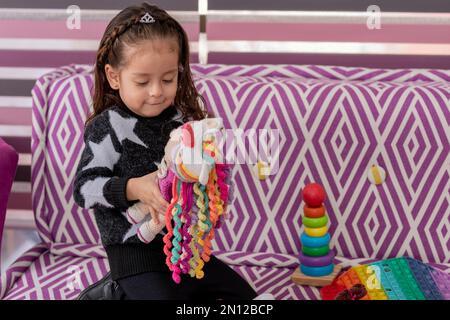 Ein Mädchen spielt mit einer Puppe, die auf der Couch einer Kinderarztpraxis sitzt und Platz zum Kopieren hat. Stockfoto