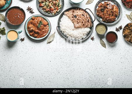 Indisches Buffet mit ethnischen Speisen auf weißem Beton mit Blick auf den Tisch: Curry, Samosa, Reis, Biryani, Dal, Paneer, Chapatti, Naan, Hühnchen Tikka Masala, Mangomädchen Stockfoto