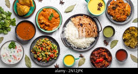 Indisches Ethnic Food Buffet auf weißem Betontisch von oben: Curry, Samosa, Reis Biryani, Dal, Paneer, Chapatti, Naan, Hühnchen Tikka Masala, Mango la Stockfoto