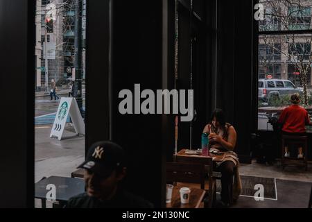 Ein Gast sah, wie er in der Innenstadt von Starbucks Seattle mit einem Schild mit dem Starbucks Logo auf der Straße Essen aß. Starbucks hat bekannt gegeben, dass sein Coffee House am Broadway und Denny in Capitol Hill, Seattle, aufgrund von „Sicherheitsvorfällen“ geschlossen wird. Der Standort, der das erste Starbucks-Coffee House in Seattle war, löste Kontroversen unter Mitarbeitern aus, die behaupten, die Schließung sei das Ergebnis von Taktiken gegen Gewerkschaften. Workers United, die Gewerkschaft der Arbeitnehmer, argumentiert, dass die Schließung am Jahrestag der Gründung der Gewerkschaft im letzten Jahr und am Capitol Hill Store geplant sei Stockfoto