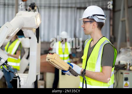 Junger weißer Ingenieur, der die Fernsteuerung mit einem Automatik-Roboterarm für die Produktion in der Fabrik verwendet, Roboterelektronik an Stockfoto