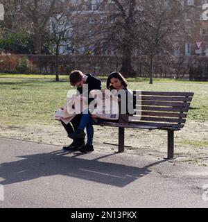Ein Paar sitzt an einem Wintertag auf einer Bank im Regents Park und liest in der Sonne Zeitungen. London, England Stockfoto