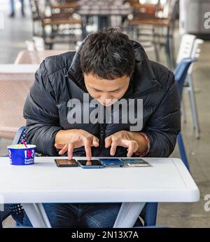 Japanischer Mann, der vier Telefone gleichzeitig abhört, spielt möglicherweise ein Spiel Stockfoto