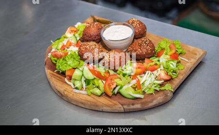 Falafel-Teller mit Gemüsesalat und Sauce auf dem Küchentisch. Stockfoto