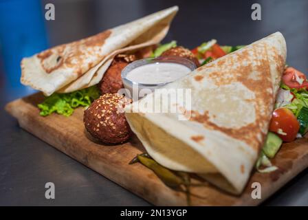 Präsentiert das libanesische Gericht Falafel im Nahen Osten auf einer Holzplatte. Tortilla, Gemüsesalat und Tahini-Sauce. Stockfoto
