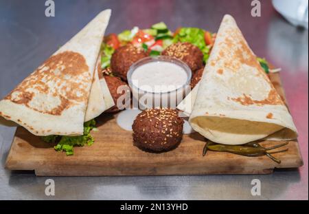 Präsentiert das libanesische Gericht Falafel im Nahen Osten auf einer Holzplatte. Tortilla, Gemüsesalat und Tahini-Sauce. Stockfoto