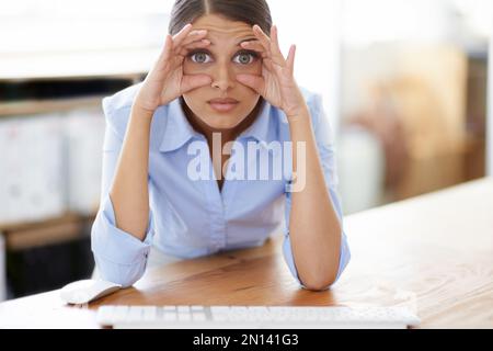 Ich bin bereit, hier einzuschlafen. Eine junge Geschäftsfrau an ihrem Schreibtisch, die versucht, ihre Augen mit den Fingern offen zu halten. Stockfoto