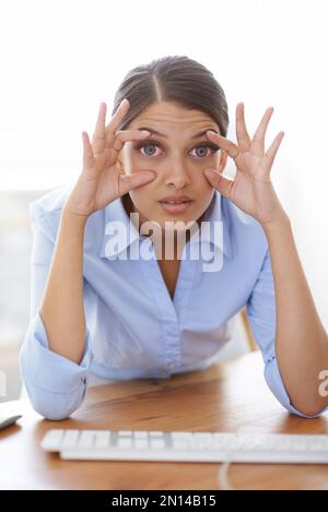 Ich war schon ewig wach. Eine junge Geschäftsfrau an ihrem Schreibtisch, die versucht, ihre Augen mit den Fingern offen zu halten. Stockfoto