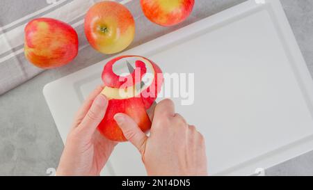 Eine Frau, die einen roten Apfel schält. Nahaufnahme von oben Stockfoto