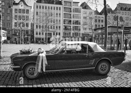 Eine Graustufenaufnahme von Gebäuden und einem Oldtimer entlang einer Straße in Köln - Straßenfotografie Stockfoto