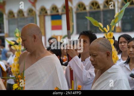 Anfängermönche, einer mit Tätowierungen auf dem Kopf, in einer Zeremonie, die durch den Tempel laufen, mit Familie und Freunden, die Schirme und Opfer tragen, Wat Ong Tue, Vienti Stockfoto