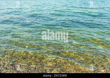 Meeressteine im Meerwasser. Kieselsteine unter Wasser. Die Aussicht von oben. Nautischer Hintergrund. Sauberes Meerwasser. Transparentes Meer. Stockfoto