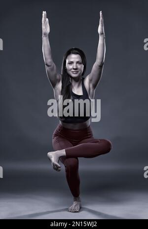 Einfarbig, wie eine Yoga-Trainerin eine Power-Yoga-Pose auf grauem Hintergrund macht Stockfoto