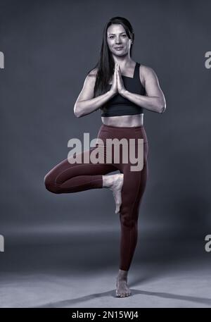 Monochrom-Ton einer Yoga-Praktizierenden in einem Vrksasana-Pose-Studio auf grauem Hintergrund Stockfoto