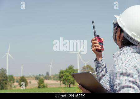 Ingenieurin kommuniziert mit dem Arbeitsteam über Walkie-Talkie bei der Installation von Windturbinen, um Elektrizität für die Gemeinde zu erzeugen. Stockfoto