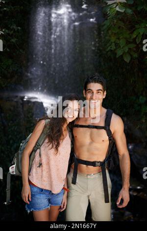 Kein Urlaub ist komplett ohne Abenteuer. Porträt eines wunderschönen jungen Paares, das an einem schattigen Ort in der Nähe eines Wasserfalls steht. Stockfoto