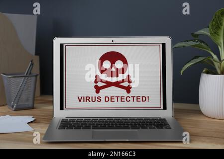 Laptop mit Warnung vor Virenangriffen auf Holztisch im Büro Stockfoto