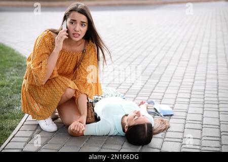 Eine Frau ruft einen Krankenwagen, um einer bewusstlosen Person mit Herzinfarkt auf der Straße zu helfen Stockfoto