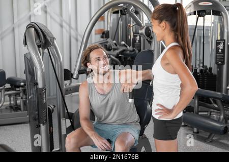 Fitnessstudio Paar fit Leute trainieren zusammen glücklich sprechende asiatische Frau und weißer Mann an den Geräten des Fitnesscenters Stockfoto