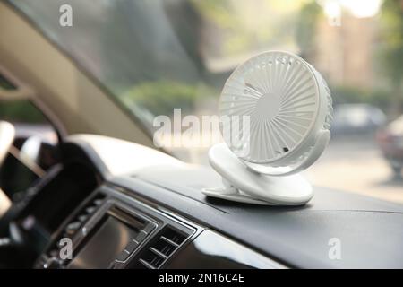 Tragbarer Ventilator auf dem Armaturenbrett im Auto. Sommerhitze Stockfoto