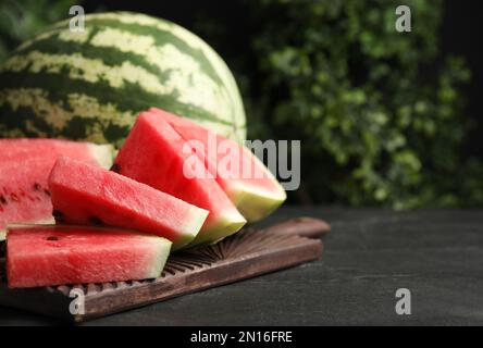 Ganze und geschnittene reife Wassermelonen auf schwarzem Tisch. Platz für Text Stockfoto