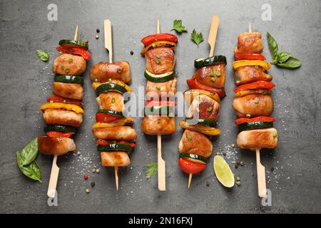 Köstliche Hähnchen-Shish-Kebabs mit Gemüse und Kräutern auf grauem Tisch, flach liegend Stockfoto