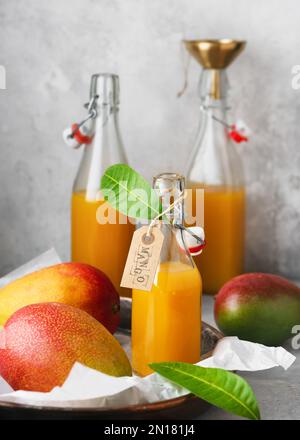 Hausgemachter Mangosaft in einer Glasflasche auf einem Metalltablett mit frischen, reifen Früchten. Gesundes Sommeressen- und Getränkekonzept. Selektiver Fokus. Speicherplatz kopieren. Stockfoto