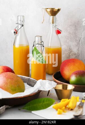 Köstlicher Mangosaft in Glasflaschen mit frischen, reifen Früchten und Blättern. Konzept für hausgemachte Bio-Lebensmittel. Speicherplatz kopieren. Stockfoto