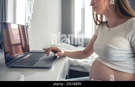 Eine junge schwangere Frau verwendet zu Hause ein Notebook. Stockfoto