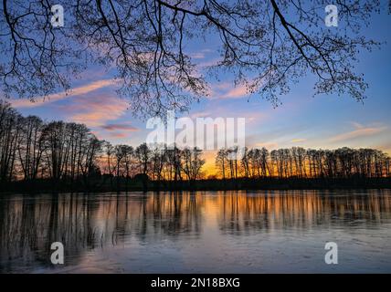 Lietzen, Deutschland. 05. Februar 2023. Der Sonnenuntergang scheint farbenfroh über einem kleinen See im Osten Brandenburgs und spiegelt sich im Eis auf dem Wasser wider. Zu Beginn der Woche erwarten in Berlin und Brandenburg niedrige Temperaturen und vereiste Bedingungen in einigen Gegenden. Wie der deutsche Wetterdienst (DWD) am Montag angekündigt hat, beginnt die Woche mit leichtem Schneefall in Teilen von Berlin und Brandenburg. D Kredit: Patrick Pleul/dpa/Alamy Live News Stockfoto