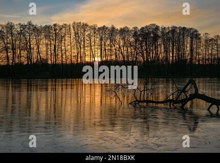 Lietzen, Deutschland. 05. Februar 2023. Der Sonnenuntergang scheint farbenfroh über einem kleinen See im Osten Brandenburgs und spiegelt sich im Eis auf dem Wasser wider. Zu Beginn der Woche erwarten in Berlin und Brandenburg niedrige Temperaturen und vereiste Bedingungen in einigen Gegenden. Wie der deutsche Wetterdienst (DWD) am Montag angekündigt hat, beginnt die Woche mit leichtem Schneefall in Teilen von Berlin und Brandenburg. D Kredit: Patrick Pleul/dpa/Alamy Live News Stockfoto