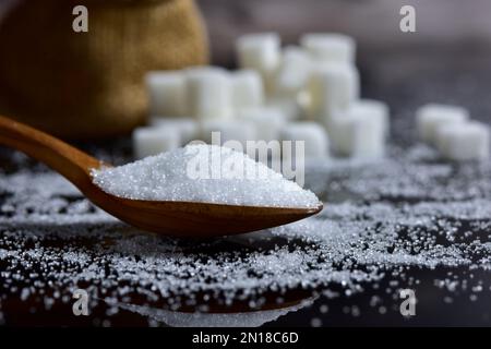 Der Zuckerguss, der sich aus Holzlöffeln und Zuckerwürfeln auf schwarzem Hintergrund in die Form des Hügels stapelt. Selektiver Fokus. Stockfoto