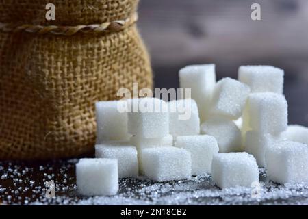 Weißzuckerwürfel und raffinierter Zucker in Leinensack auf schwarzem Hintergrund. Selektiver Fokus. Stockfoto