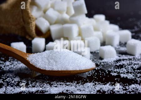 Der Zuckerguss, der sich aus Holzlöffeln und Zuckerwürfeln auf schwarzem Hintergrund in die Form des Hügels stapelt. Selektiver Fokus. Stockfoto