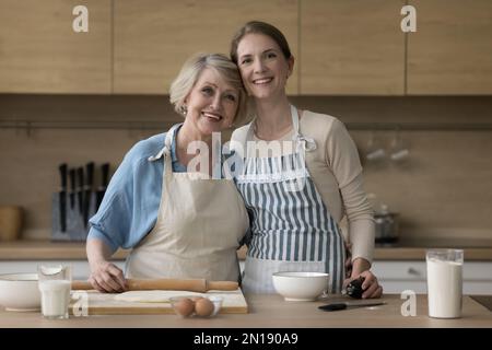 Fröhliche, reife Mutter und Erwachsene Tochter, die am Tisch backen Stockfoto
