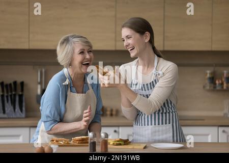Aufgeregte Seniormutter und glückliche Erwachsene Tochter, die Sandwiches zubereitete Stockfoto