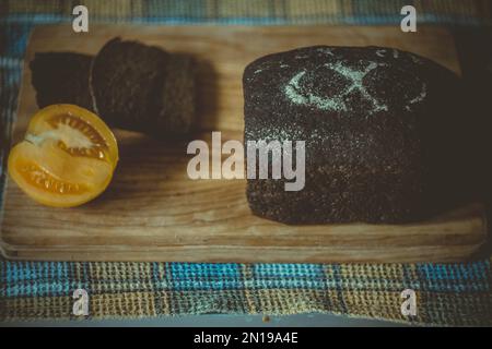 Nahaufnahme von hausgemachtem Roggenbrot und halber Tomate auf dem Schneidebrett Konzeptfoto Stockfoto