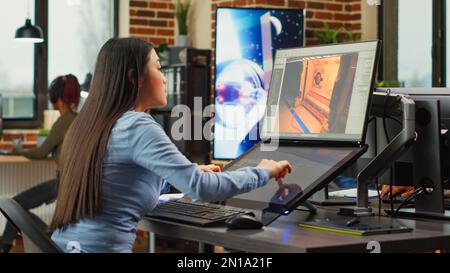 Asiatischer Spieleentwickler, der in der Produktionsabteilung arbeitet, um professionelle Inhalte mithilfe des Touchscreens zu erstellen. Experte für die Entwicklung von 3D-Szenen und -Grafiken mit professioneller Software. Stockfoto