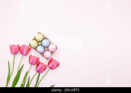 Rosafarbene Tulpen mit Korb mit farbigen Eiern in einer Ecke mit Platz für Text. Ostern. Pastellfarbener Hintergrund. Speicherplatz kopieren Stockfoto