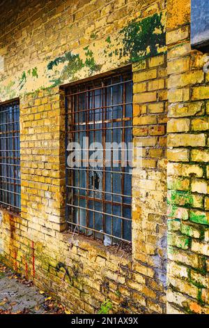 Alte Gitterfenster mit zerbrochenem Glas an der Außenwand eines alten verlassenen Fabriklagers Stockfoto