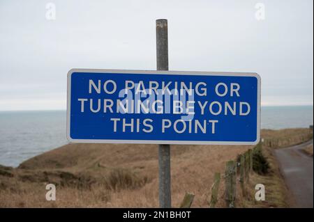 Schild „Parken verboten“ oder „Wenden verboten“ über diesen Punkt hinaus. Unscharfer Hintergrund von Landstraßen, Zäunen, Feldern und Meer. Stockfoto