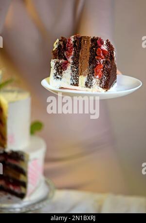 Das Mädchen schneidet und serviert ein Stück Kuchen. Festliche Hochzeit zweistufiger Kuchen mit frischen Blumen dekoriert Stockfoto