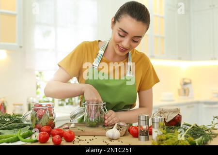 Eine Frau, die Dill am Tisch in der Küche in ein Essigglas steckt Stockfoto