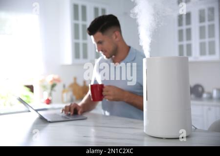 Mann mit Laptop in der Küche mit modernem Luftbefeuchter Stockfoto