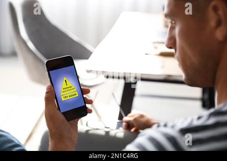 Mann mit Smartphone mit Warnung vor Virenangriff zu Hause, Nahaufnahme Stockfoto