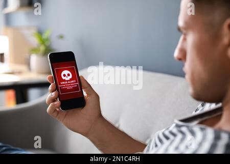Mann mit Smartphone mit Warnung vor Virenangriff zu Hause, Nahaufnahme Stockfoto