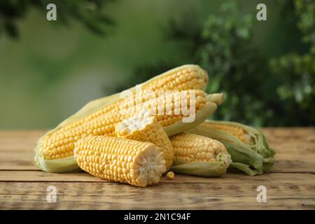 Reife rohe Maiskolben auf Holztisch vor unscharfem Hintergrund Stockfoto