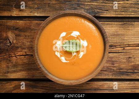 Leckere cremige Kürbissuppe mit Basilikum in der Schüssel auf einem Holztisch, Draufsicht Stockfoto